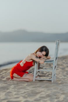 Woman in Red Dress Resting Head on Wooden Chair on Beach